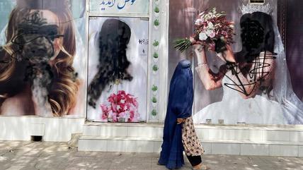 A veiled woman walks past a beauty parlour. The faces of the women on the adverts on the wall are painted over in black.