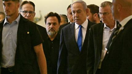 Netanyahu in the centre of the picture, walking surrounded by men in suits in the Knesset.