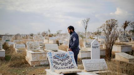 رجل يرتدي الزي العسكري يقف وسط مقبرة للمسلمين في حلب. (photo: Picture Alliance / Middle East Images | B. Alhammoud) رجل يرتدي الزي العسكري يقف بين مقبرة للمسلمين.
