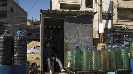 A man sells fuel from plastic bottles on the road in Syria