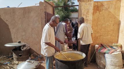 Local initiative providing food to refugees. Khartoum, April 2024 (Photo: Picture Alliance / Xinhua News Agency | M. Khidir) A man ladles food from a large pot. Women stand in a queue in the background.