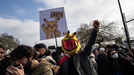 A crowd of people at a demo. One man is wearing a pikachu helmet with reflective visor.