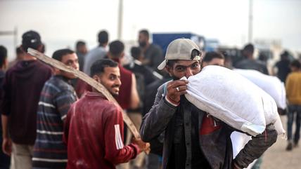 وصول الدقيق إلى مدينة غزة، 10 يونيو/حزيران 2025. (Photo: Picture Alliance / NurPhoto | M. Fathi) رجل يرتدي قبعة بيسبول يحمل كيسًا من الدقيق ويقبله.