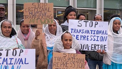 Women in traditional Eritrean clothing hold up signs reading: "Stop Criminal Human Trafficking Network"