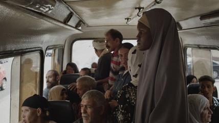 Die Hauptdarstellerin steht in einem öffentlichen Minibus, um sie herum andere Passagiere.