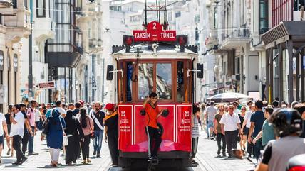 Ein kleiner Junge zeigt den Daumen nach oben, er fährt hinten auf einer roten Tram durch eine belebte Straße.