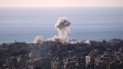 A plume of smoke rises from a building in a dense Beirut neighbourhood. The sea and the sky are in the background.