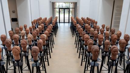 In einer Galerie sind Tonfiguren von Köpfen in Reihen angeordnet.