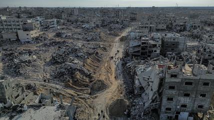 An aerial view of destroyed buildings with people walking among the rubble.
