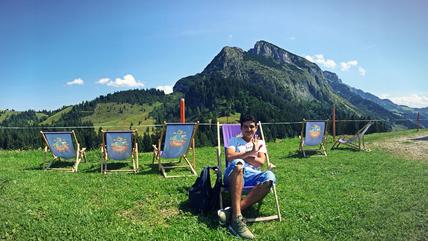 Ein Junge in Jeans sitzt in einem Sonnenstuhl vor einer Bergkulisse