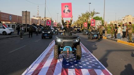 Members of Iraq's Popular Mobilization Forces carry a portrait of Ayatollah Ali Khamenei as they ride over a U.S. flag in Baghdad, Oct. 1, 2026. (Photo: picture alliance / AP Photo/Hadi Mizban | Hadi Mizban)