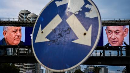 A road sign with two arrows pointing to the faces of Eisenkot and Netanyahu shown on large billboards in the background..