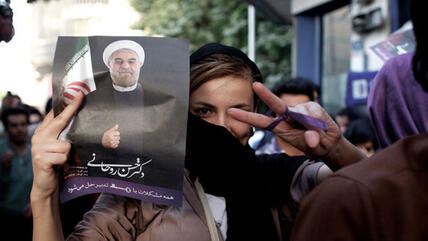 An Iranian woman flashes the sign for victory as she holds a portrait of Hassan Rouhani during celebrations after he won the Islamic Republic's presidential elections in Tehran on 15 June 2013 (photo: Behrouz Mehri/AFP/Getty Images)