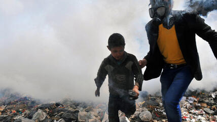 A man wearing a gas mask and a boy run away from a combat zone in Aleppo, Syria (photo: Getty Images/AFP)