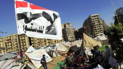 Anti-Mursi protesters sit outside their tents, below a flag that reads, ''No to the Constitution'' at Tahrir Square in Cairo, 10 December 2012 (photo: Reuters)