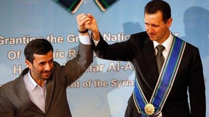 In this Oct. 2, 2010 file photo, Iranian President Mahmoud Ahmadinejad, left, holds up the hand of his Syrian counterpart Bashar Assad after he awarded Iran's highest national medal to Assad, in a ceremony in Tehran, Iran (photo: AP)
