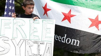 An exiled Syrian boy in the USA holds up a placard bearing the words ''Free Syria'' (photo: Reuters)