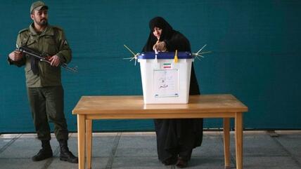 A woman casting her vote in Tehran, a military soldier with machine gun standing guard (photo: Reuters)