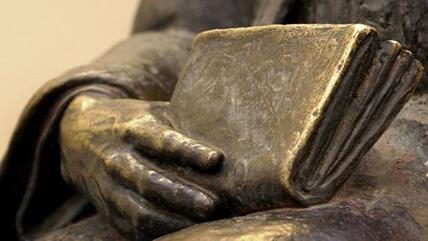 Close-up of a statue of a person holding a book (photo: Bilderbox)