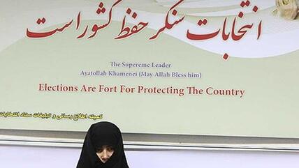 A woman stands in front of a poster declaring that elections in Iran are for the protection of the country (photo: Mehr)