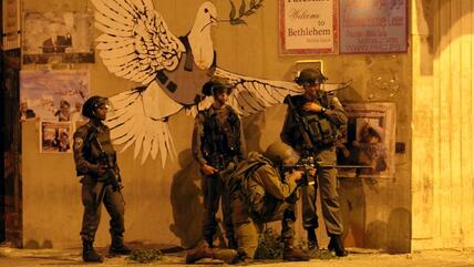 مجموعة من الجنود  يطلقون  النار  على شبان  يحتجون على الحرب في غزة  من تحت شعار "حمامة السلام"  رسمة على مدخل مدينة بيت لحم -تصوير مهند حامد