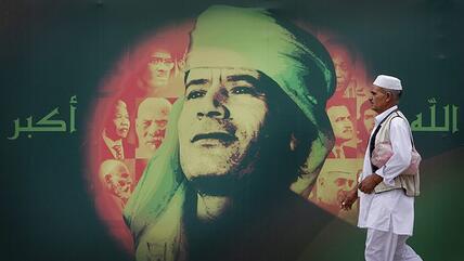 Libyan man passes billboard of Gaddafi′s face and the Arabic tag ″God is great″, Tripoli 2009 (source: AP/Ben Curtis)