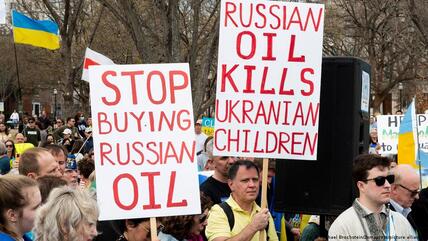 أشخاص يحملون لافتات تقول "توقفوا عن شراء النفط الروسي" و "النفط الروسي يقتل الأطفال الأوكرانيين" في مسيرة لدعم أوكرانيا أقيمت أمام البيت الأبيض.