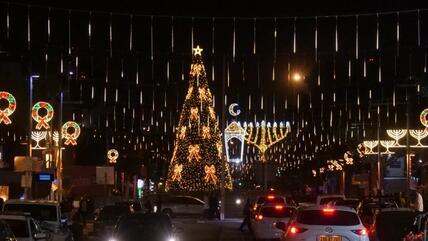 شجرة عيد الميلاد مضاءة بجانب ثريا عيد حانوكا في حيفا. 
