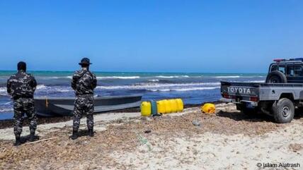 Two armed men on an eastern Libyan beach guard a boat that was used to carry migrants (photo: Islam Altarash)
