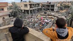 Two boys wearing anoraks look down from a balcony onto buildings destroyed in Israeli airstrikes on Gaza