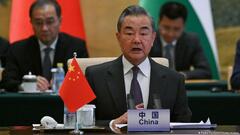 China's Foreign Minister Wang Yi sits behind a desk with a small Chinese flag. In the background are two men and a partial view of Chinese and Palestinian flags