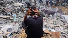 A child sits with his head in his hands as people salvage belongings from the rubble of a damaged building following strikes on Rafah, Gaza Strip, 12 November 2023