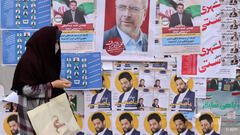 A woman walks in front of a wall bearing electoral posters in Tehran