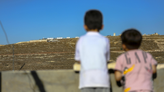 Zwei kleine Jungen schauen von einem Hausdach auf Siedlungen im Westjordanland