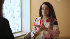 Eine Frau in bunter Bluse sitzt vor einem Fenster und spricht mit ihrem Gegenüber.