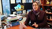 Wearing a headscarf, Amaney Jamal sits at her desk in an office strewn with books and papers. In the background are two monitors and book shelves