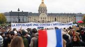 Thousands of people stand in a public square. Someone holds up a French flag and in the background, people hold a banner saying: "The Republic united against anti-Semitism"