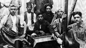A black and white image of a group of seated Afghan musicians posing with their instruments in Kharabat, Kabul