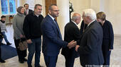 Ahmed Abunada in suit and glasses shakes hands with German President Frank-Walter Steinmeier (right), amidst a group of people waiting to be greeted