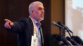 Hamas leader Yahya Sinwar gesticulates while speaking into a banl of microphones, a Palestine band draped around his neck