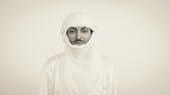  الموسيقي النيجيري بومبينو. صورة من Ron Whyman A man (Nigerien Musician Oumara Moctar/Bombino) dressed entirely in a white traditional Tuareg outfit and headdress against a white backdrop
