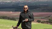 Wearing sunglasses, Reuters journalist Issam Abdallah stands on a grassy slope; a flat plain with fields, trees and settlements can be seen behind him