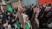 Men and women, some wearing green Hamas scarves or holding up Hamas flags, point their right index fingers in the air at a rally in April 2022