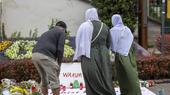 A man and two women wearing headscarves stand in front of a memorial plaque for the victims of the knife attack in Solingen.