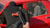 Ein Mann mit Gewehr beugt sich zum offenen Fenster eines roten Autos.
