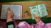Two people point their fingers at two copies of the Qur'an. Photo from above, only the hands visible.