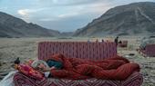 Eine alte Frau liegt auf einem Sofa, das in einer steinigen Landschaft steht.