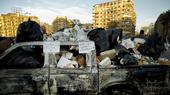 A burnt out truck full of trash bags. On the window frame a sign reads "Here lies Mubark's government!"