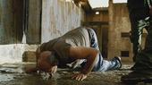 A man gets down on his knees, licking water.