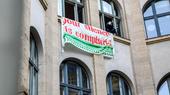 The facade of a building with a sign hanging from the windows reading "Your silence is complicity"